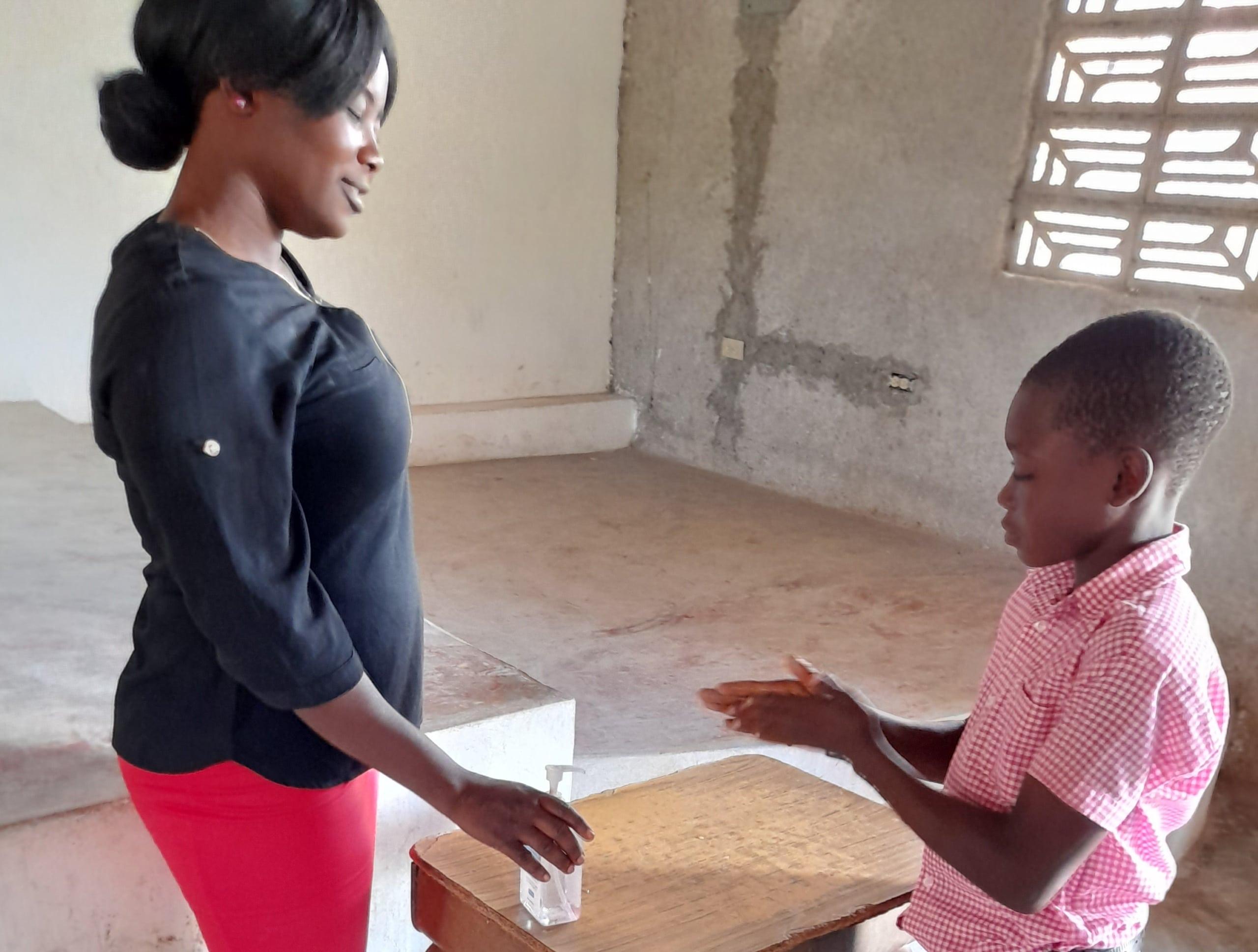 A school teacher talking to one of her students about the importance of keeping their hands clean - Oranger, Haiti.